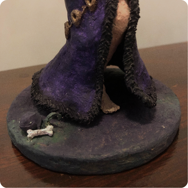 Close-up of the sculpture’s base with a purple dress and small bone detail.