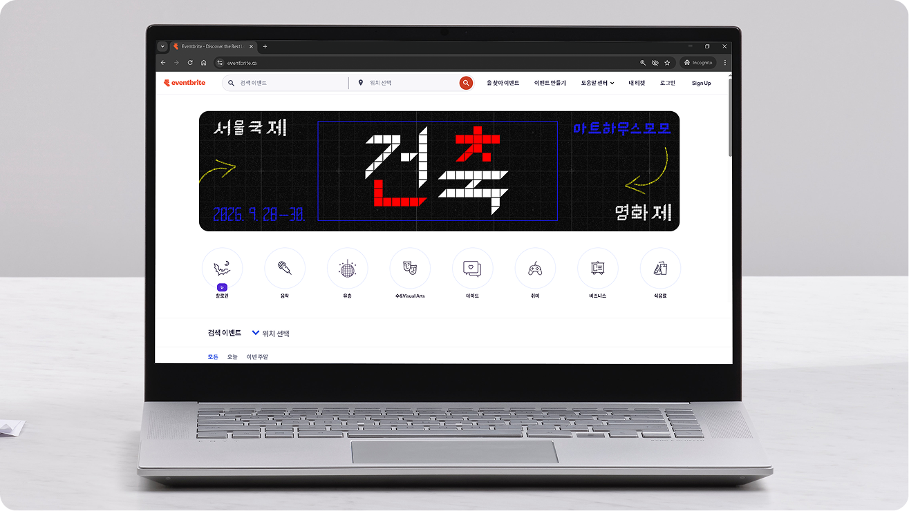 Laptop displaying a Korean film festival website homepage with bold grid-based typography, dates, and navigation icons on a dark background.