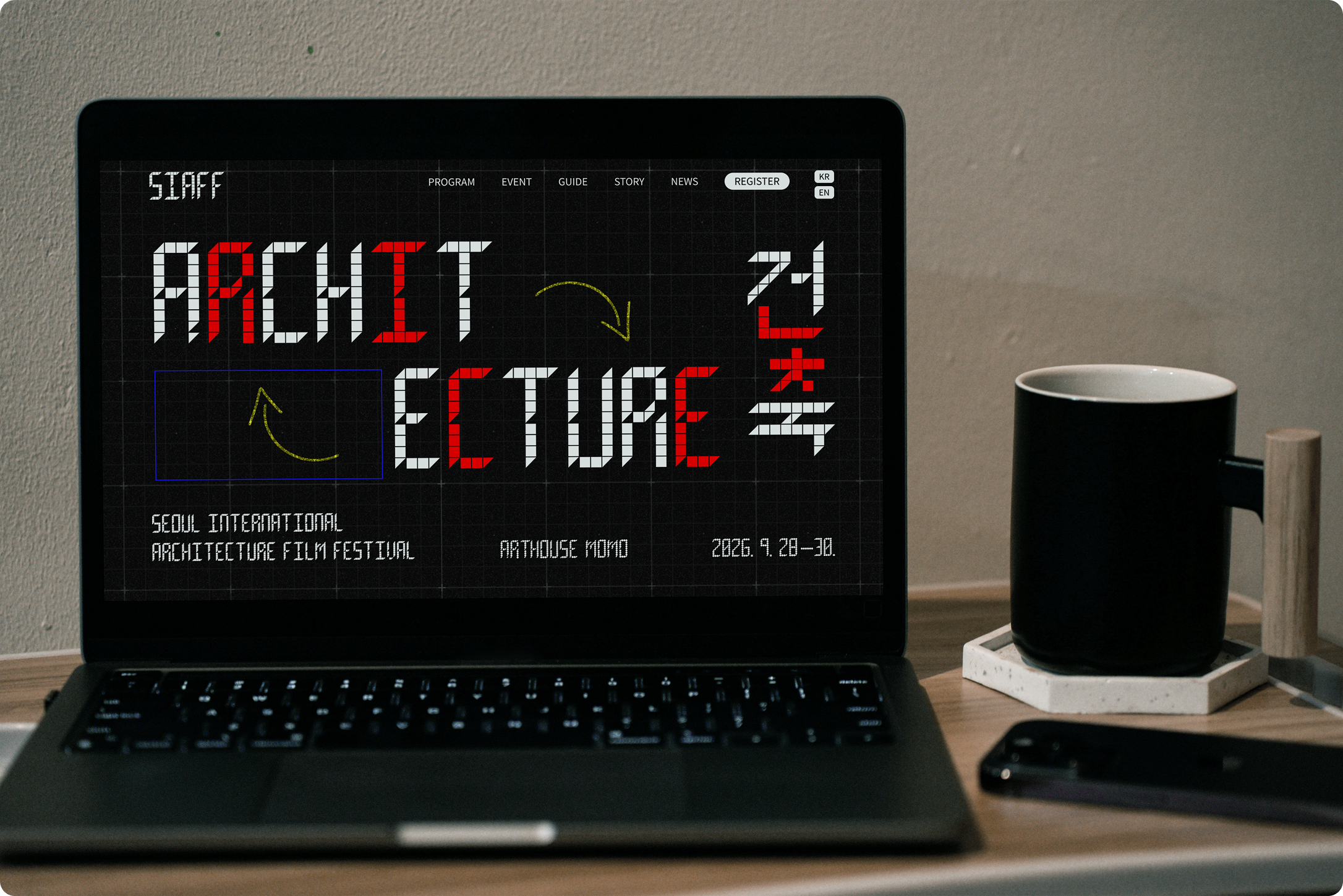 Laptop on a desk displaying a dark-themed festival website with large block lettering reading “ARCHIT ECTURE,” red accents, and event details for the Seoul International Architecture Film Festival.